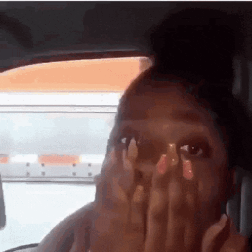 a woman with long nails is sitting in a car covering her face with her hands .