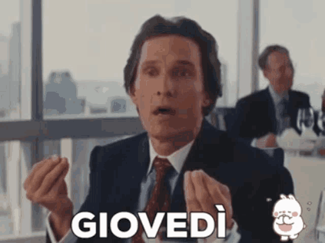a man in a suit and tie is sitting at a table with the word giovedi in front of him .