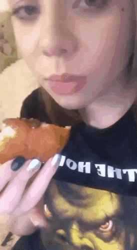 a woman wearing a shrek t-shirt is eating a piece of pizza .