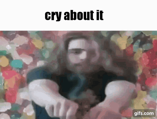 a man with long hair is sitting in front of a painting with the words cry about it .