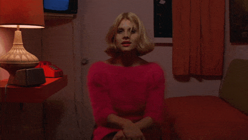 a woman in a pink sweater is sitting on a bed with the words is this your first visit here