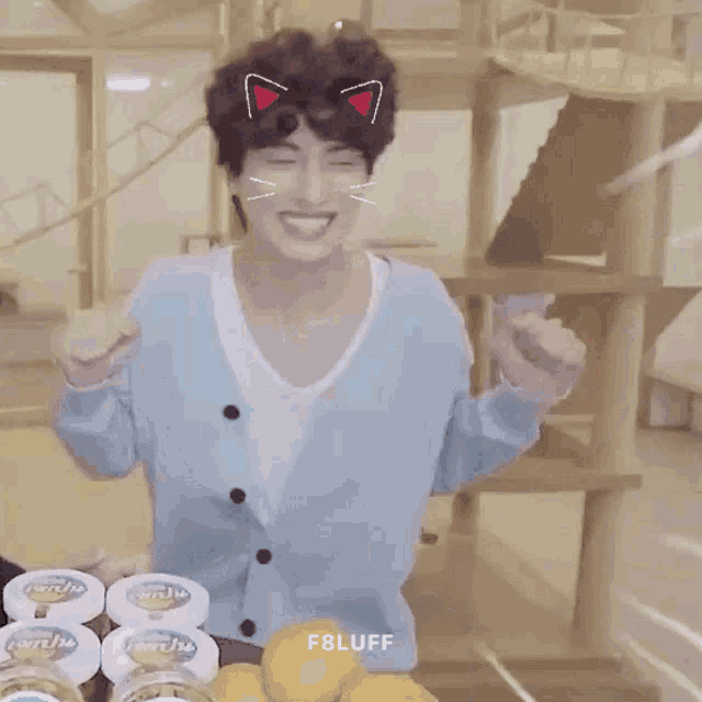 a man in a blue cardigan with cat ears on his head is standing in front of a table full of food .
