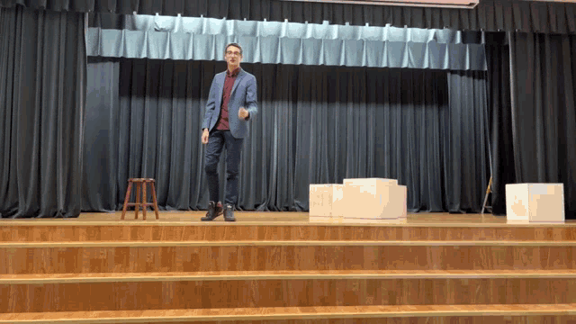 a man in a suit stands on a stage with a stool in front of him