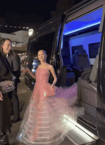 a woman in a long pink dress is getting out of a black van