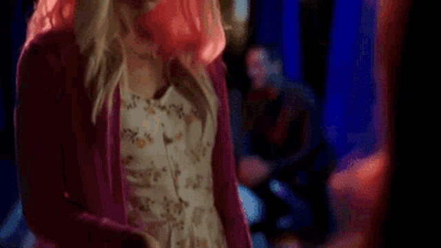 a woman with pink hair is standing in a dark room looking down .