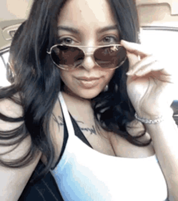 a woman wearing sunglasses and a white tank top is taking a selfie