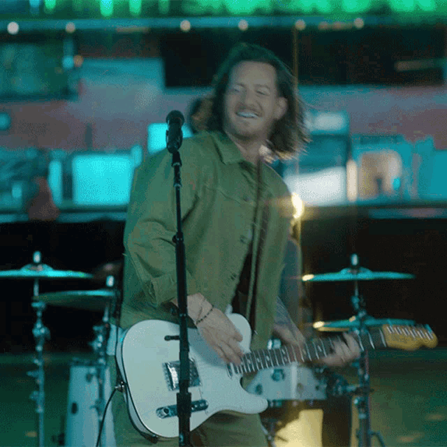 a man in a green jacket is playing a guitar and singing into a microphone