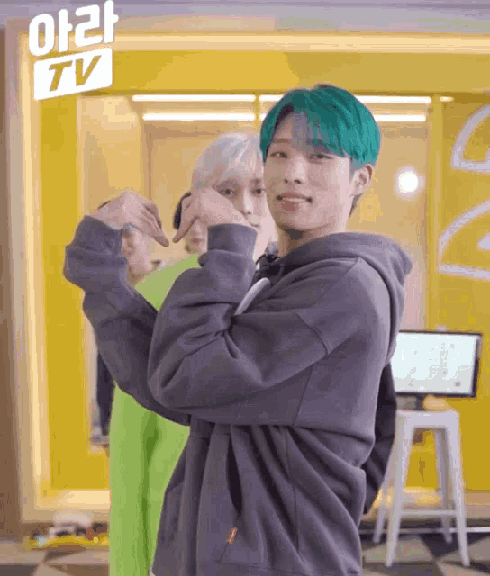 a boy with green hair is making a heart shape with his hands in front of a sign that says tv