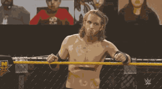 a shirtless wrestler stands in a wrestling ring with the letters w on the ring