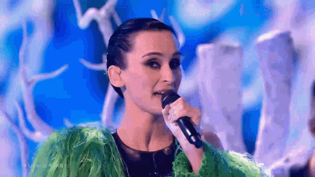 a woman is singing into a microphone while wearing a green jacket .
