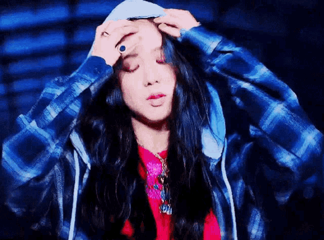 a woman wearing a blue plaid shirt and a hoodie is adjusting her hair .