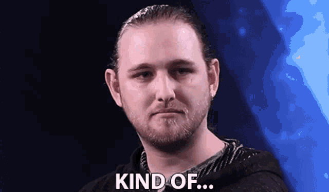 a man with a beard is standing in front of a blue background and says `` kind of ... '' .