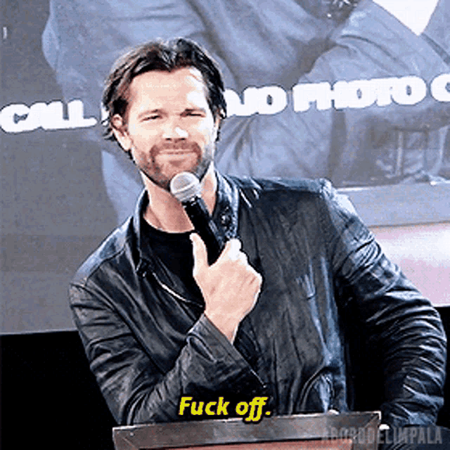 a man in a leather jacket is holding a microphone and saying " fuck off "