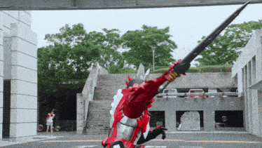 a man in a red armor is holding a large sword in front of a building