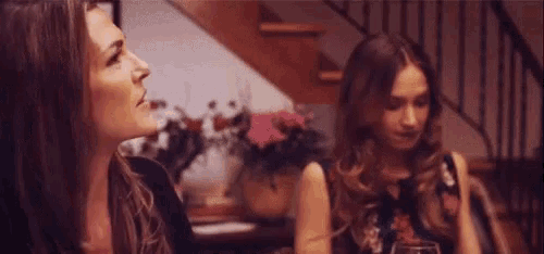 two women are sitting at a table talking to each other in a room .