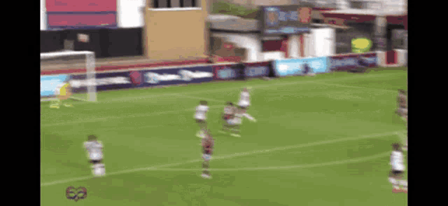 a blurry picture of a soccer game with a few players in the foreground and a few advertisements in the background