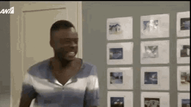 a man in a blue shirt is standing in front of a wall with pictures on it .