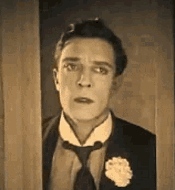 a man in a tuxedo and tie is looking out of a doorway .