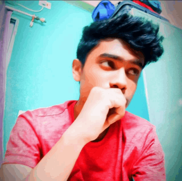 a young man covering his mouth with his hand while wearing a red shirt