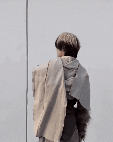 a man wearing a scarf and gloves stands in front of a wall