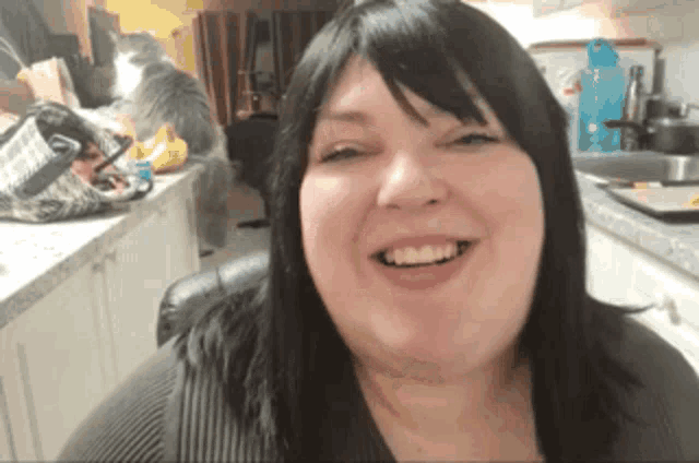 a woman with black hair is smiling in front of a cat