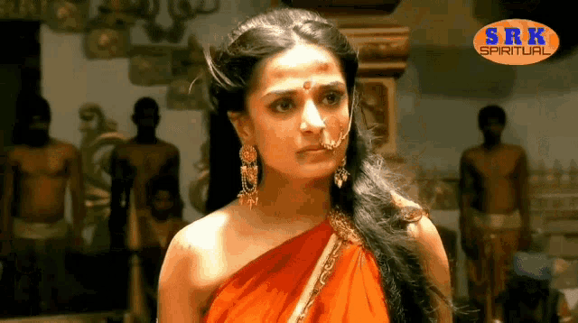 a woman in a red dress with a nose ring and earrings is standing in front of a group of men .