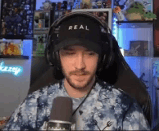 a man wearing headphones and a hat that says real is sitting in front of a microphone .