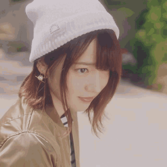 a woman wearing a white beanie and a gold jacket looks to the side