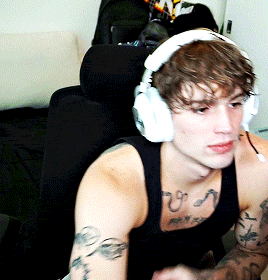 a man wearing headphones and a black tank top has a tattoo on his chest that says ' u '