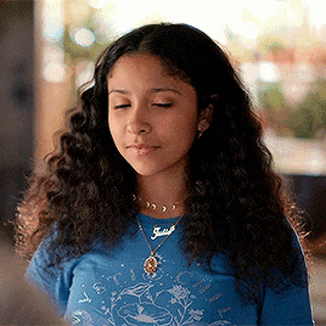 a young woman with curly hair is wearing a blue shirt and a necklace with the name julia on it .