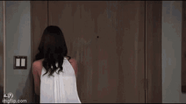 a woman in a white top is standing in front of a door with imgflip.com written on the bottom