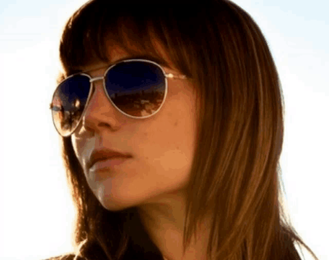 a woman wearing sunglasses has a reflection of a city in her sunglasses