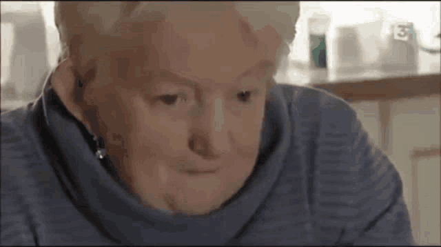 an elderly woman in a blue sweater is looking down at something