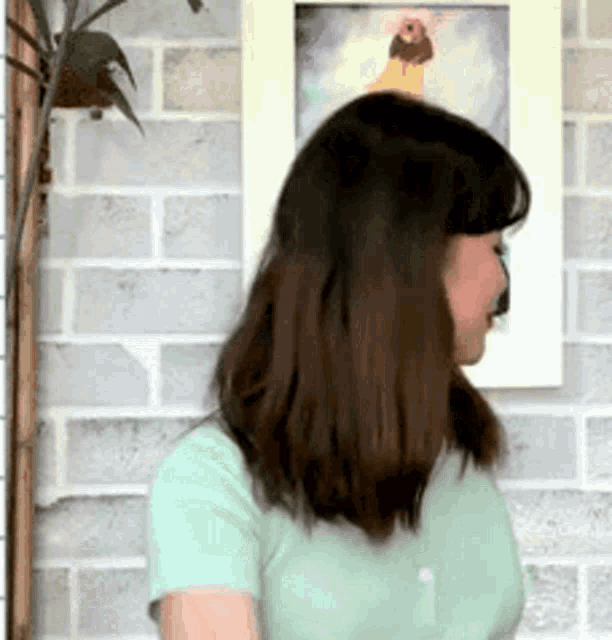 a woman in a green shirt is standing in front of a brick wall with a picture on it
