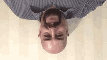 a bald man with a beard is laying upside down on a white surface .