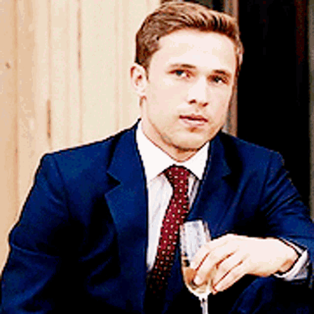a man in a suit is holding a glass of wine