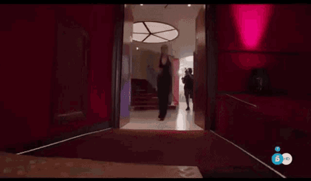 a woman in a black dress is walking down a red carpeted hallway
