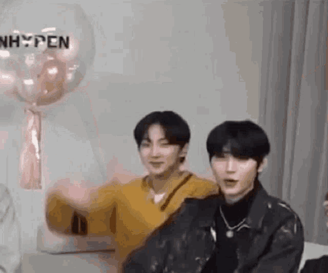 two young men are sitting next to each other in a room with balloons in the background .