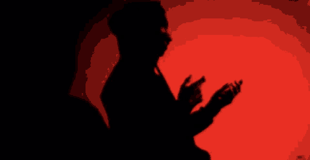 a silhouette of a man standing in front of a red background holding a cell phone .