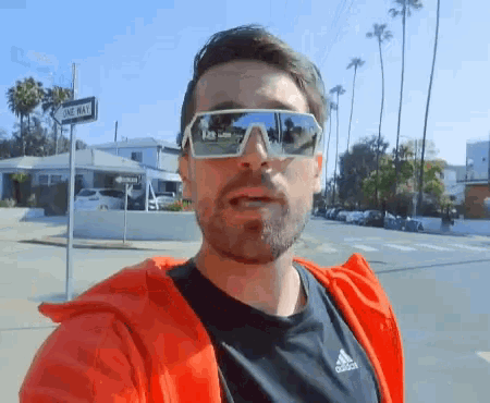 a man wearing sunglasses stands in front of a one way street sign