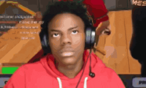 a man wearing headphones and a red hoodie is sitting in front of a computer screen .