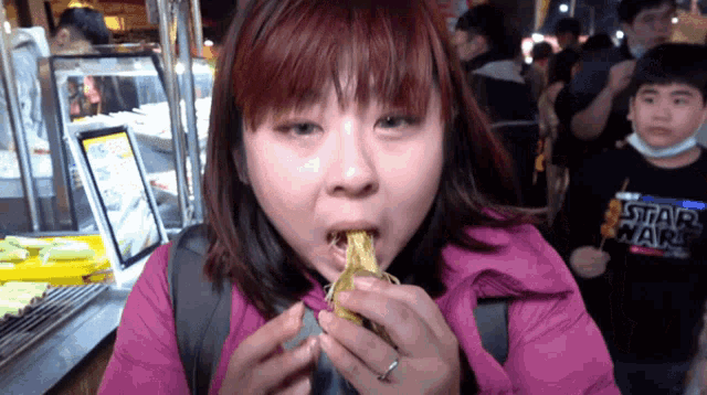 a woman in a pink jacket is eating a banana while wearing a star wars shirt