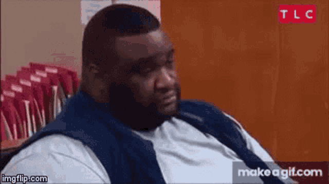 a very fat man is sitting in front of a stack of red envelopes .