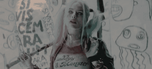 a woman in a harley quinn costume is holding a sword and a stick .
