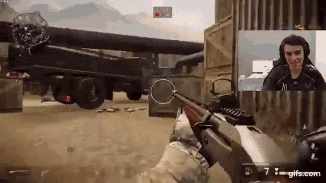 a man is playing a video game with a rifle and a truck is behind him .