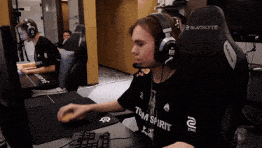 a man wearing headphones and a shirt that says team spirit sits in front of a computer