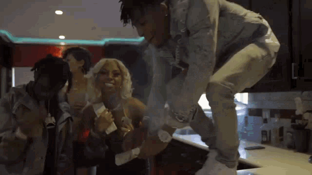 a group of people are dancing in a kitchen while a man stands on a counter .