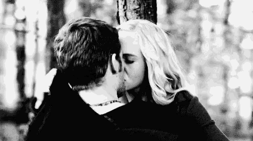 a black and white photo of a man and woman kissing in the woods .
