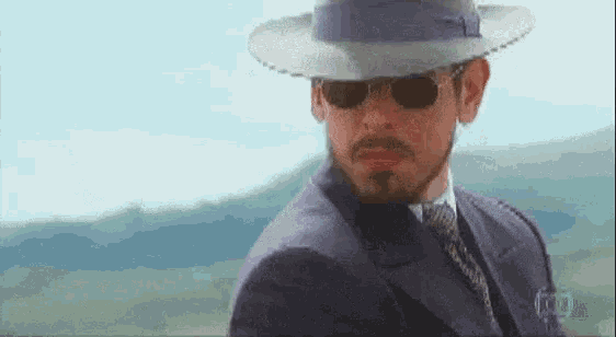 a man wearing a hat and sunglasses looks to his left