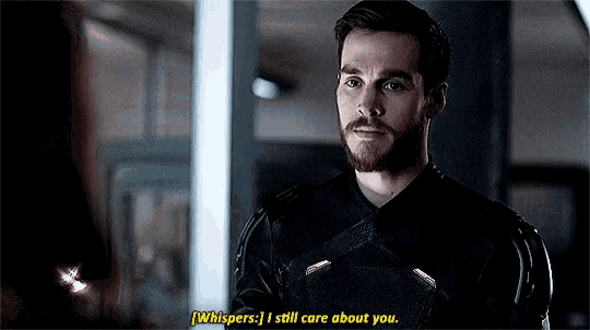 a man with a beard is talking to another man while wearing a black suit and gloves .